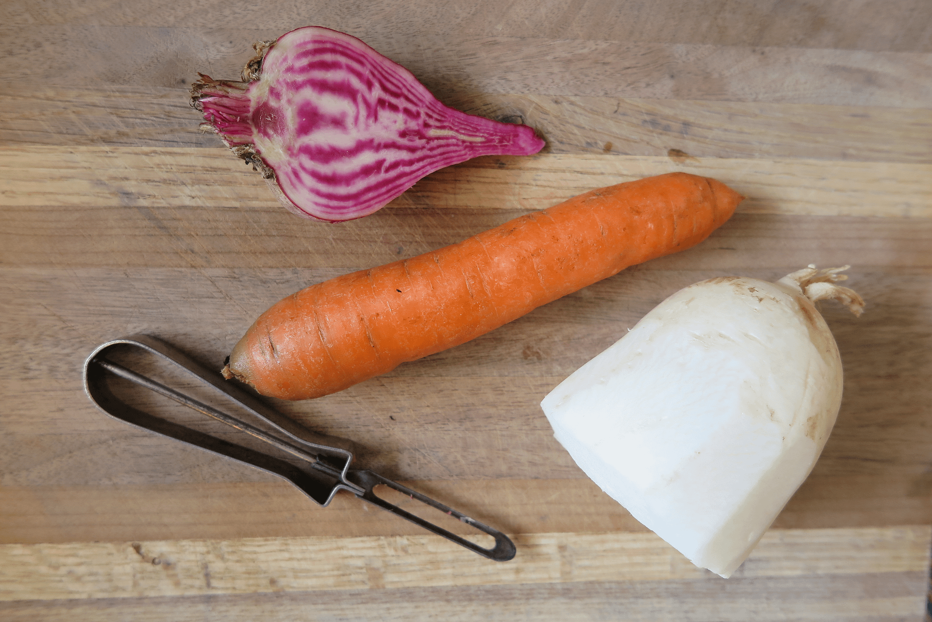 Two types of radishes and a carrot laying on a wooden cutting board ready to be peeled and chopped