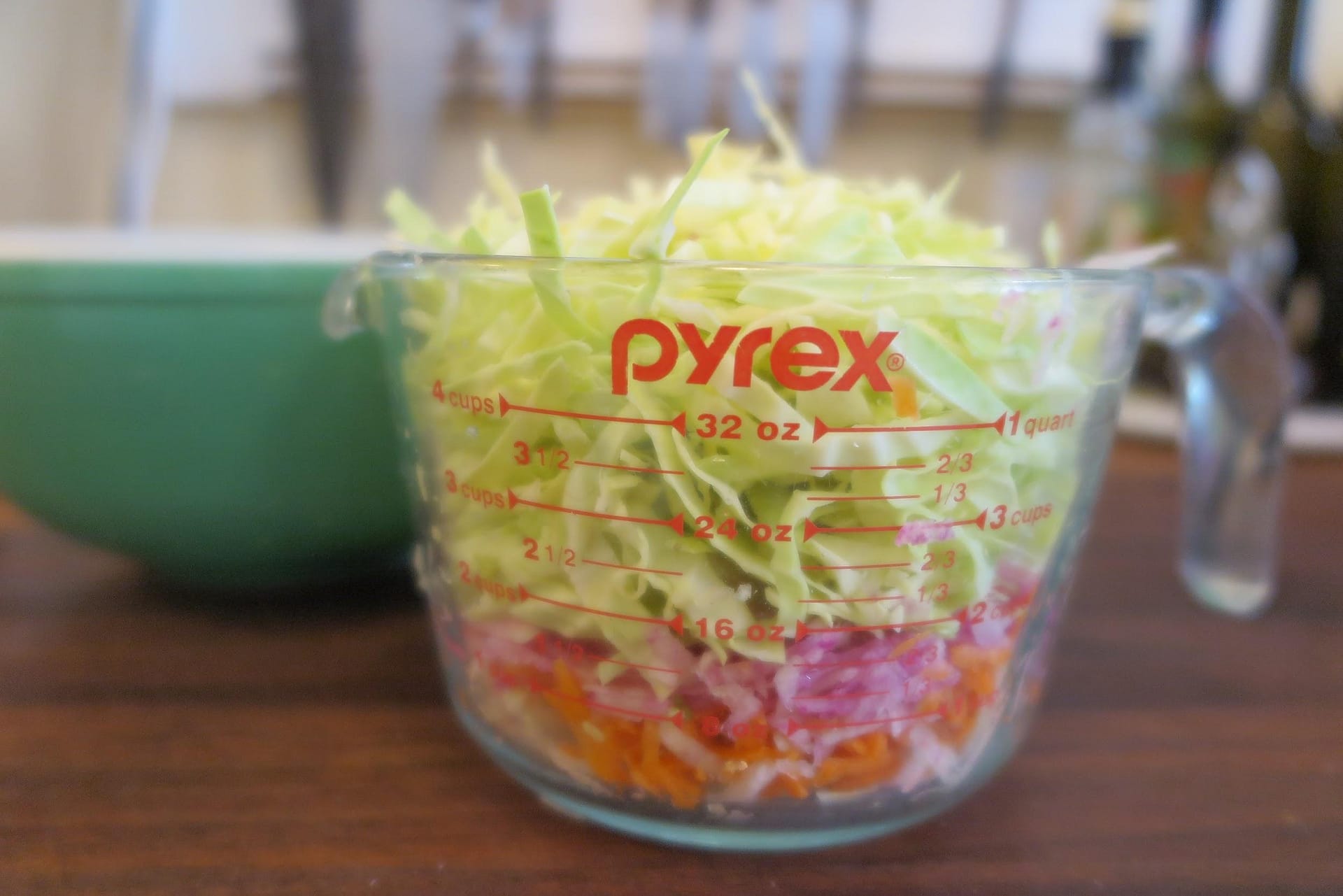 A large glass Pyrex measuring cup filled with shredded cabbage, radishes, and carrots