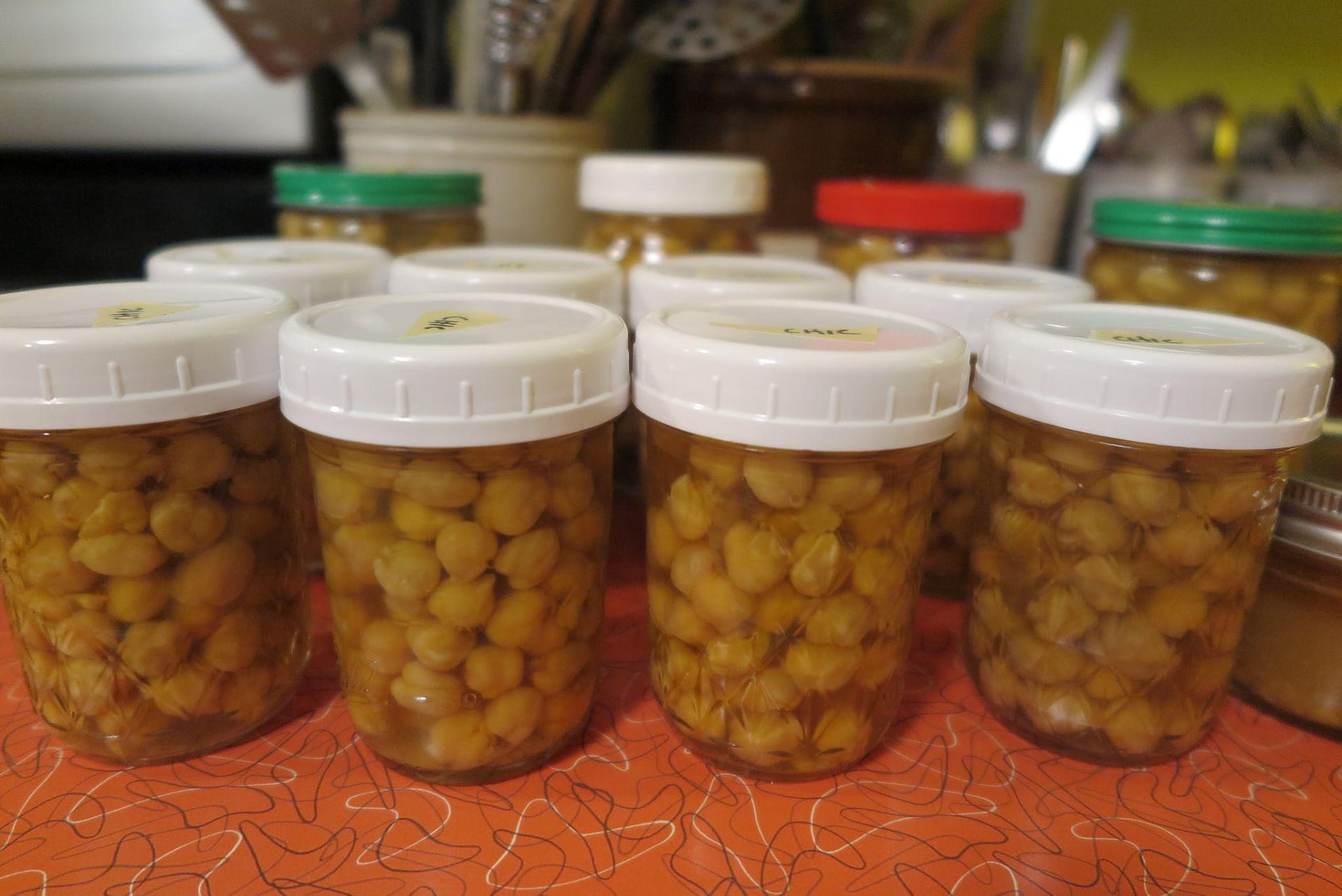 Four mason jars with white lids containing cooked chick peas