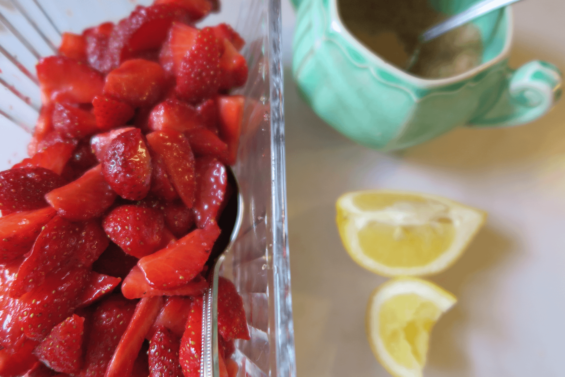 Slice strawberries in a plastic carton next lemon wedges and a light blue sugar bowl