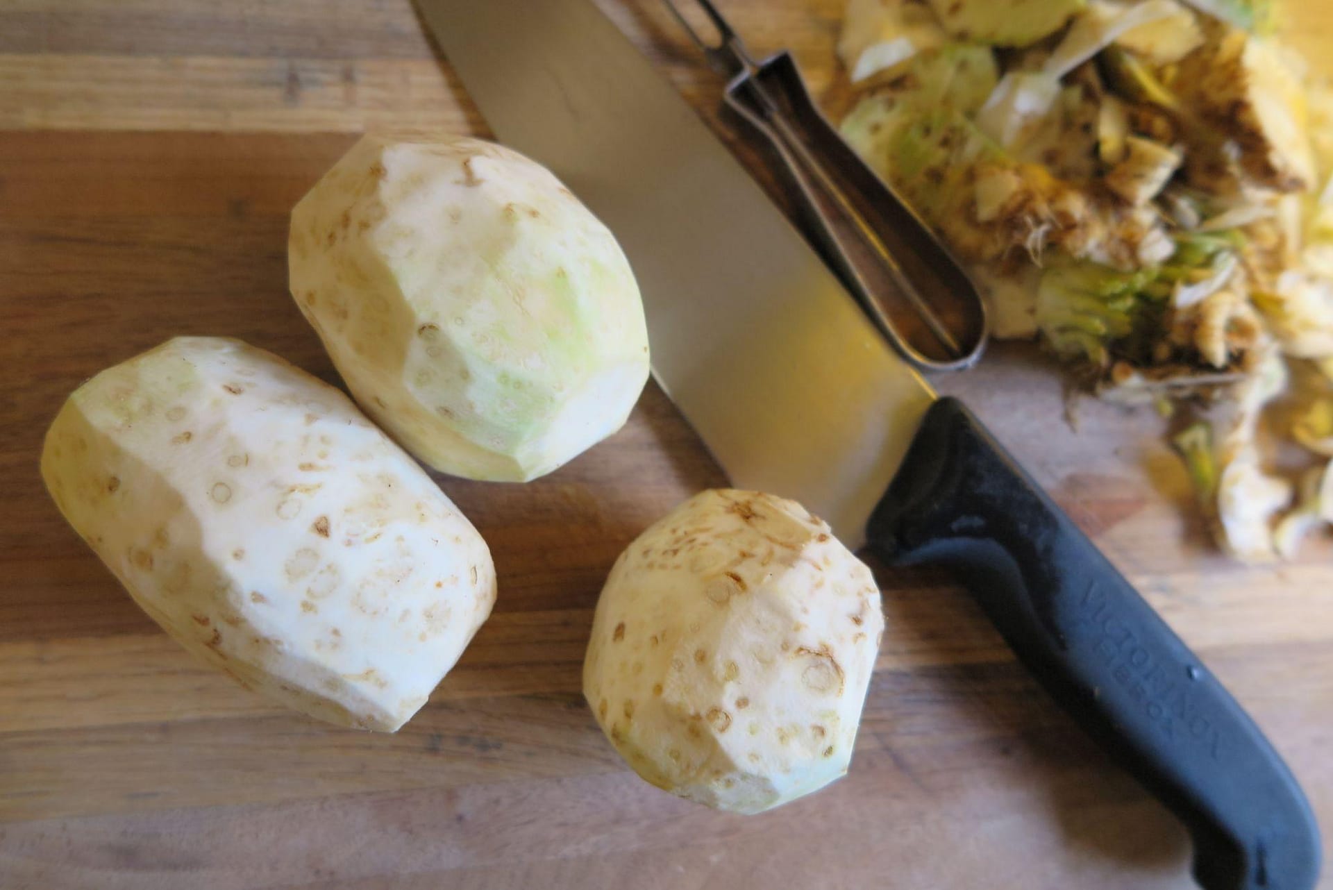 three peeled celeriacs on a cutting board next to a chef's knife and vegetable peeler