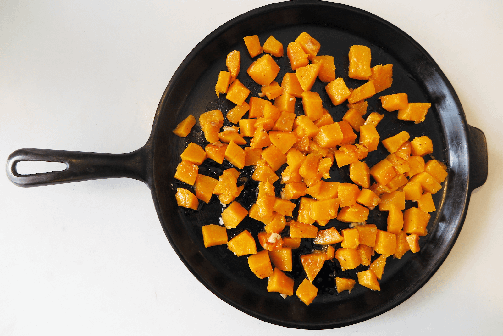 A cast iron skillet with a layer of butternut squash cubes along the bottom