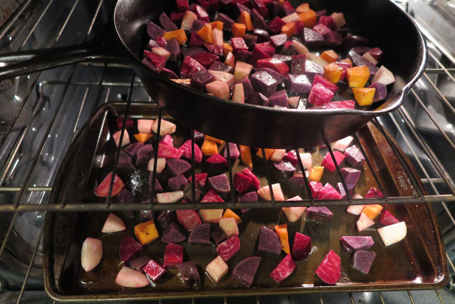Chiogga beets, sweet potatoes, turnips, and red potatoes in a cast iron skillet and on a cookie sheet in the oven ready to be roasted
